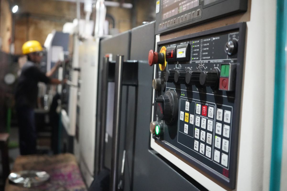 CNC lathe control panel with an operator working in the background