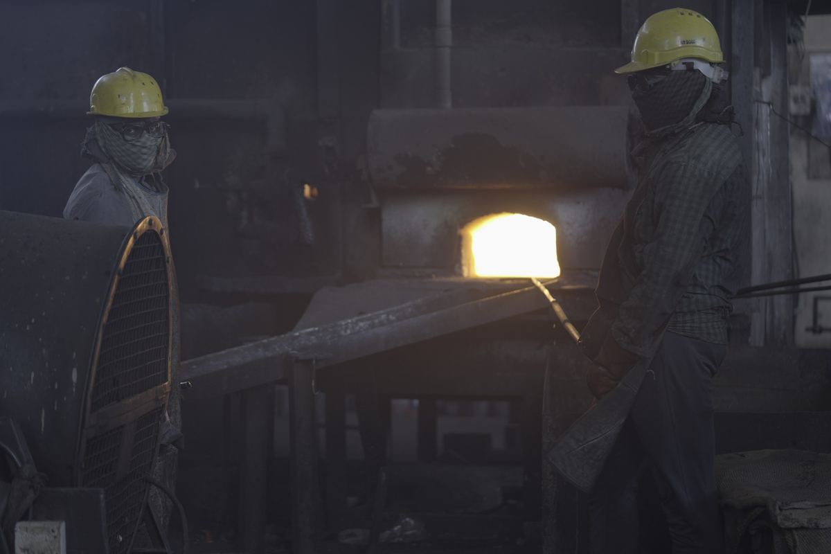 Two forging shop workers in hard hats and masks beside a glowing furnace